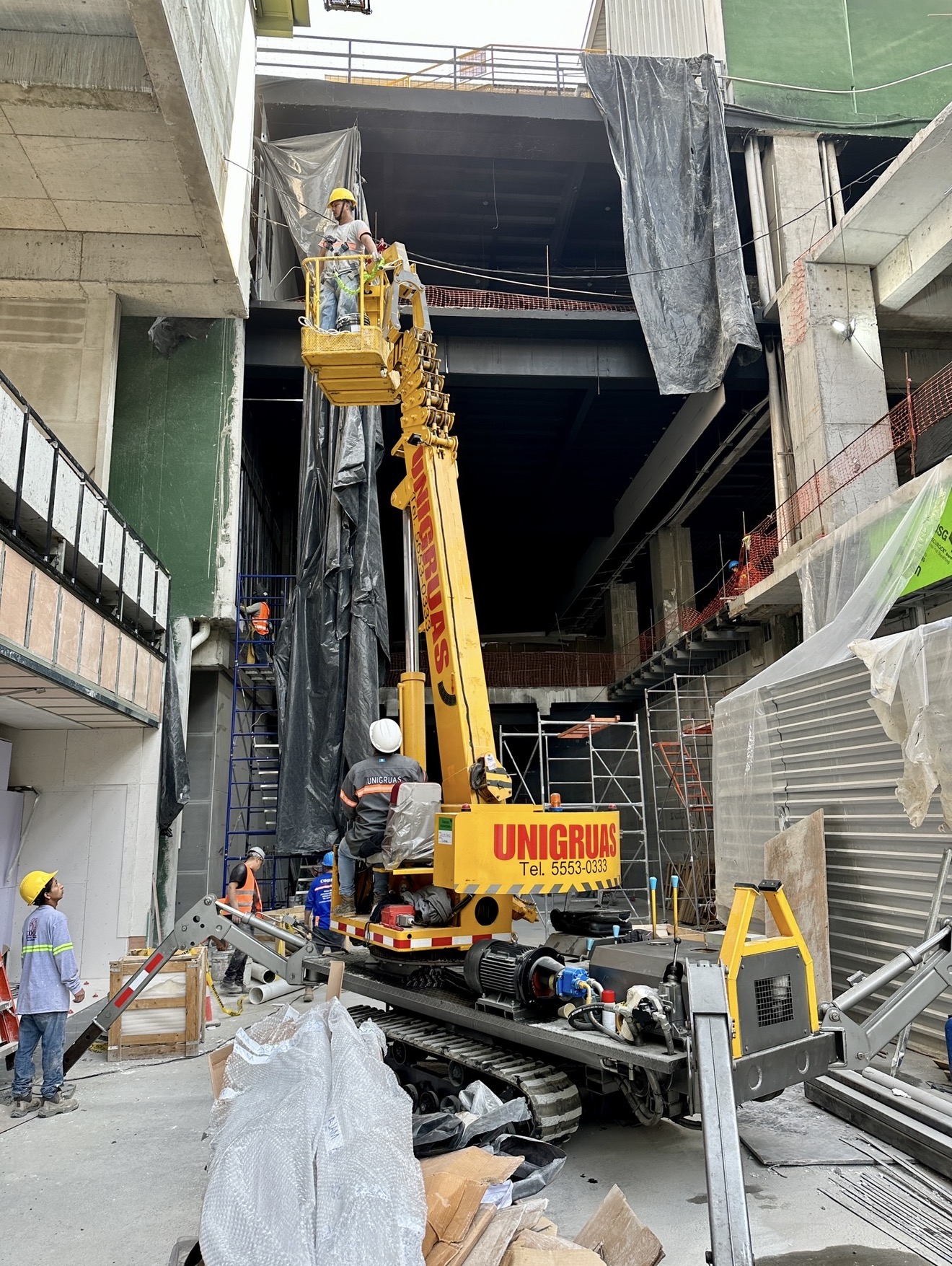 Trabajador en una canasta elevada por una grúa araña de UNIGRUAS dentro de una obra