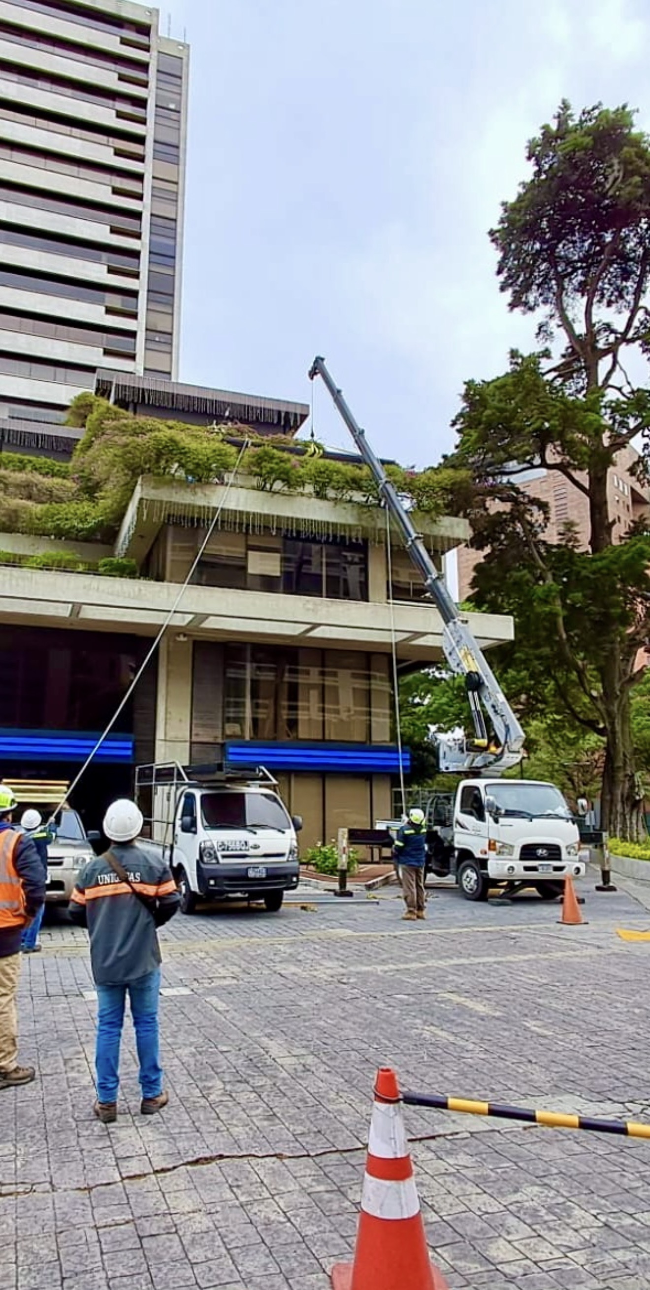Grúa de UNIGRUAS con brazo extendido durante una maniobra junto a un edificio con jardines