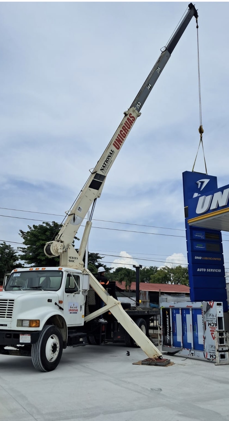 Grúa telescópica de UNIGRUAS izando un rótulo en una estación de servicio